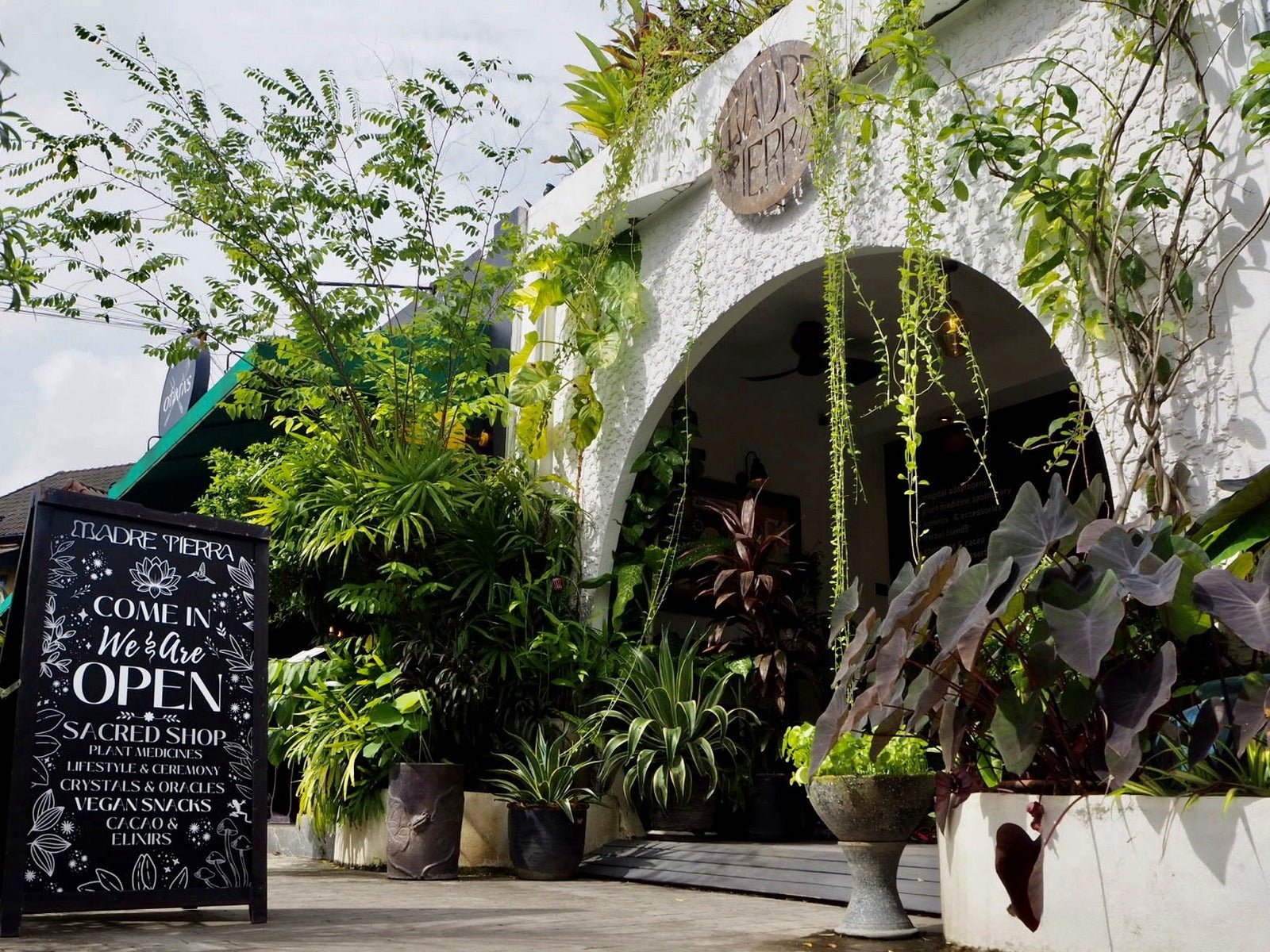 Arched storefront of Madre Tierra Apothecary in Laguna, Phuket, with plants and an open chalkboard